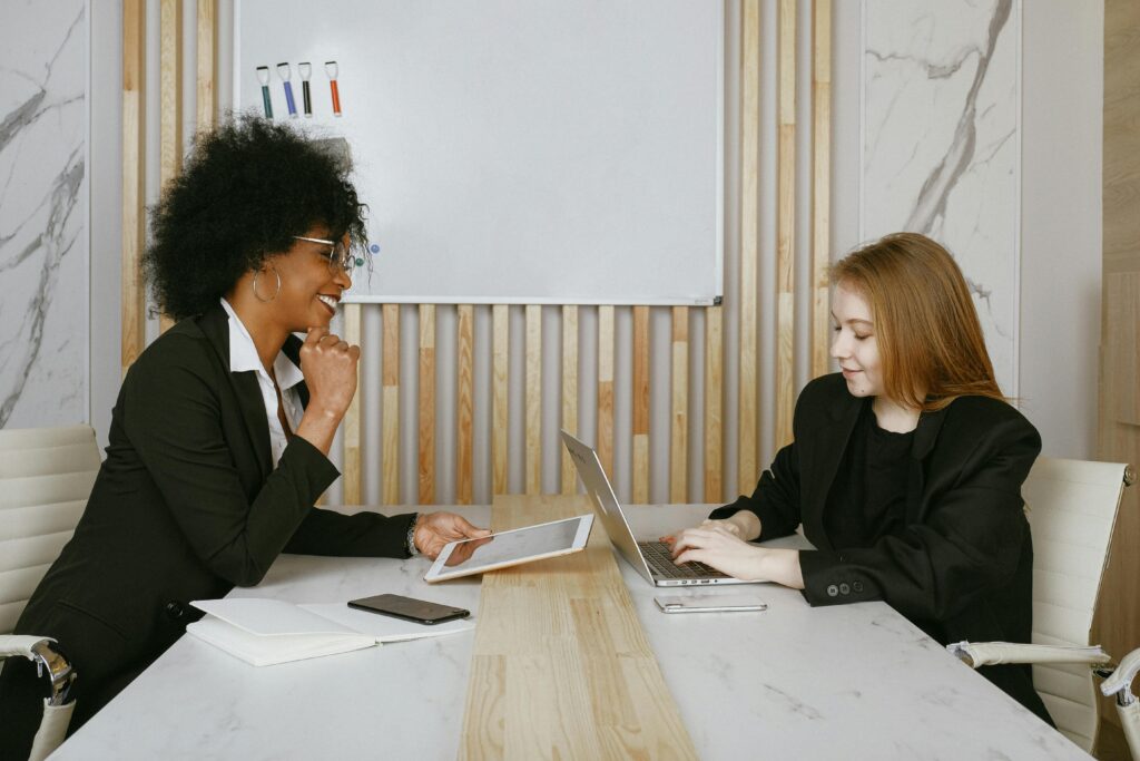 pexels-photo-3727509-3727509 Two businesswomen engaged in a meeting discussing plans using digital devices in a modern office.